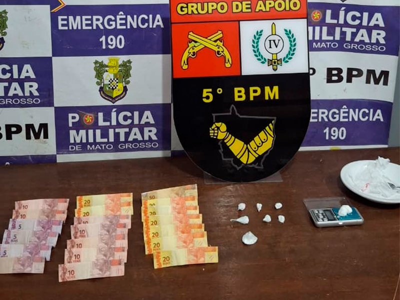 Policiais militares ao lado de um Gol vermelho e mesa com bolsas de cocaína, balança de precisão, celulares e dinheiro apreendidos na Operação Tolerância Zero em Rondonópolis