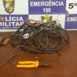 Policiais militares ao lado de fios de energia, alicate e faca apreendidos após prisão de suspeito de furto no Centro de Rondonópolis, em frente a estabelecimento comercial