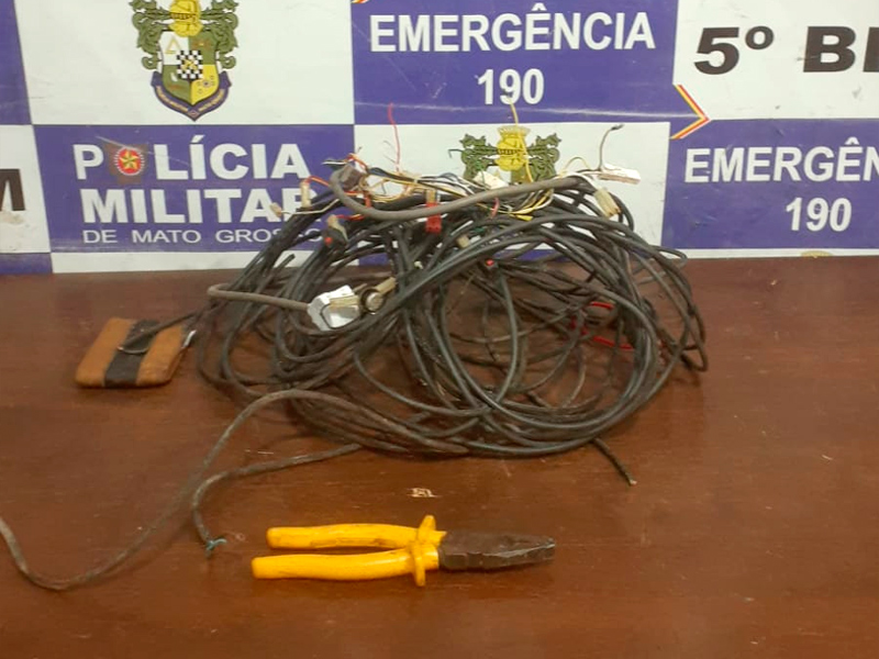 Policiais militares ao lado de fios de energia, alicate e faca apreendidos após prisão de suspeito de furto no Centro de Rondonópolis, em frente a estabelecimento comercial