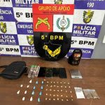 Policiais militares ao lado de viatura em rua da região central de Rondonópolis, com bolsa preta e drogas apreendidas em ação contra o tráfico de entorpecentes