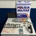 Foto de armas de fogo e porções de drogas apreendidas pela Polícia Militar sobre uma mesa.