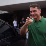 Senador Flávio Bolsonaro em entrevista coletiva, gesticulando enquanto responde sobre a eventual candidatura à Presidência em 2026 e o “preço” para desistir