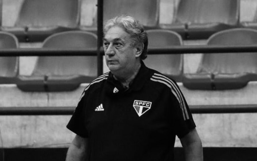 Foto do treinador Cláudio Mortari à beira da quadra orientando sua equipe durante uma partida de basquete.