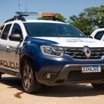 Imagem ilustrativa de uma viatura da Polícia Militar com as luzes de emergência ligadas em frente a um posto de combustíveis à noite.