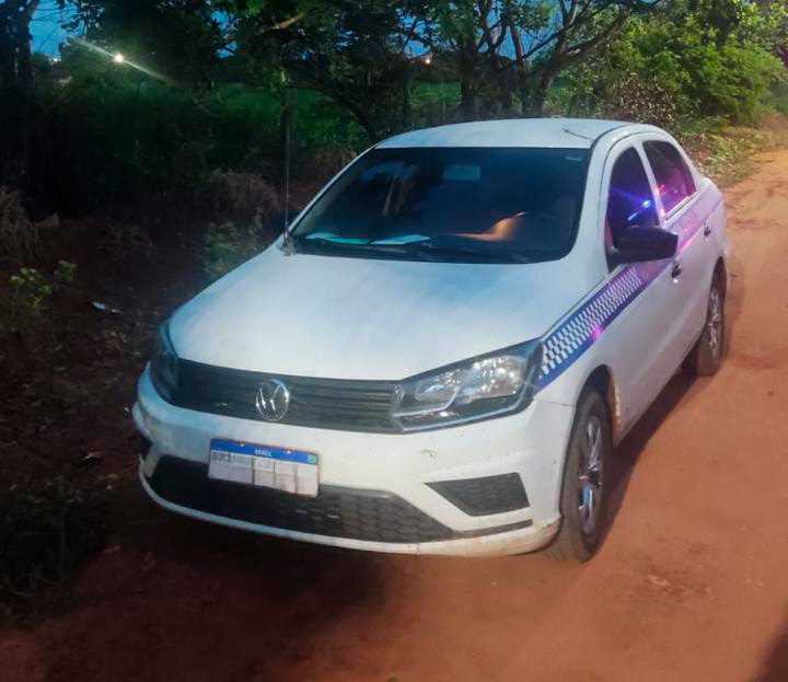 Carro branco estacionado em rua residencial com viatura da Polícia Militar ao fundo.
