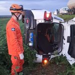 Equipe dos Bombeiros Militares realizando atendimento em veículo capotado em plantação de soja.