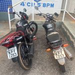 Duas motocicletas pretas idênticas estacionadas em frente à delegacia após constatação de clonagem pela Polícia Militar.