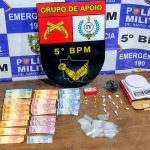 Foto exibe porções de cocaína, balança de precisão e dinheiro apreendidos pela Polícia Militar de Rondonópolis.