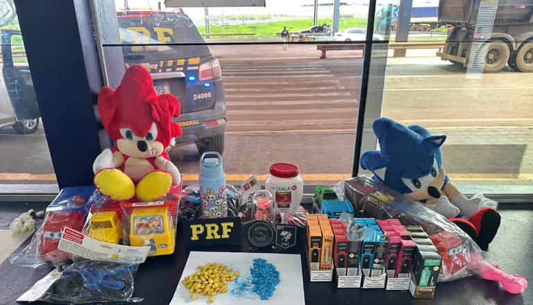 Comprimidos de ecstasy coloridos ao lado de brinquedos de pelúcia em uma mesa de apreensão da PRF.